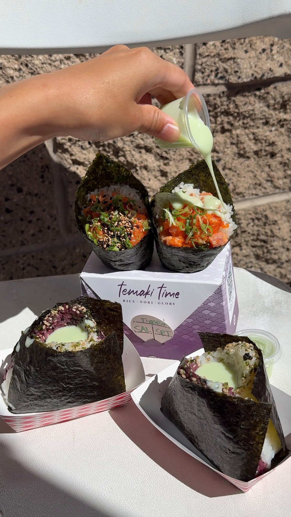 Four hand-pressed onigiri with sesame seeds and green sauce drizzle on a Temaki Time card