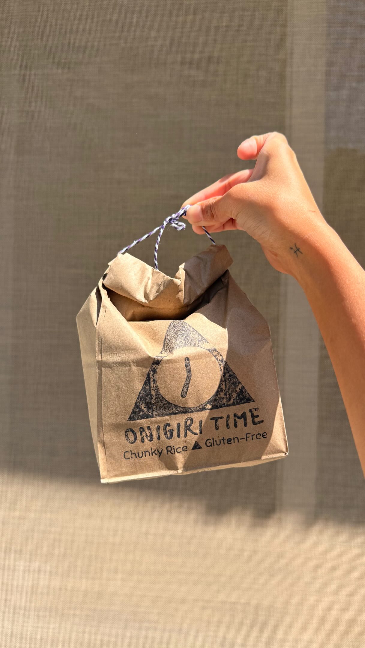 Hand holding an Onigiri Time branded paper bag with hand-stamped triangle logo